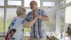 a photo of an older couple dancing in their kitchen. They are wearing normal clothes