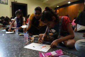 women and girls sit on the floor and draw on a piece of paper