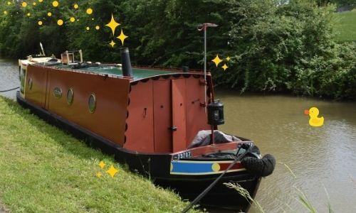 A red canal boat on water, it has sparkles coming out of its chimney and a cartoon duck sits on the water